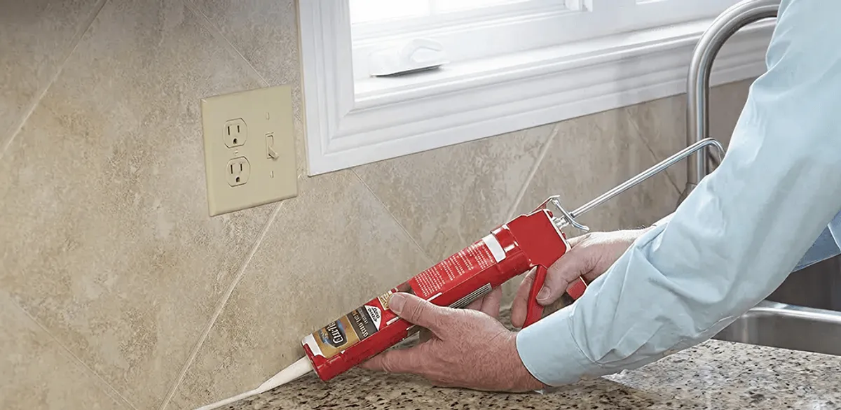 Handyman applying caulk along a kitchen backsplash and countertop seam in Manchester, NH